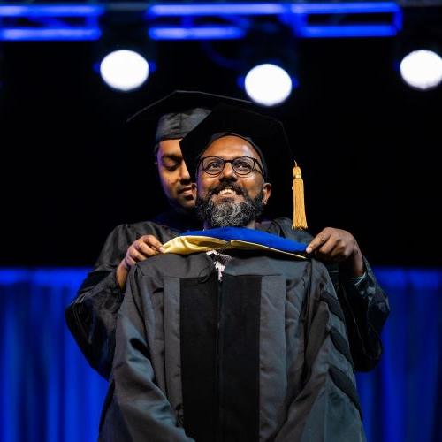 UMKC graduate student receives graduation hood from faculty member advisor during the May hooding ceremony